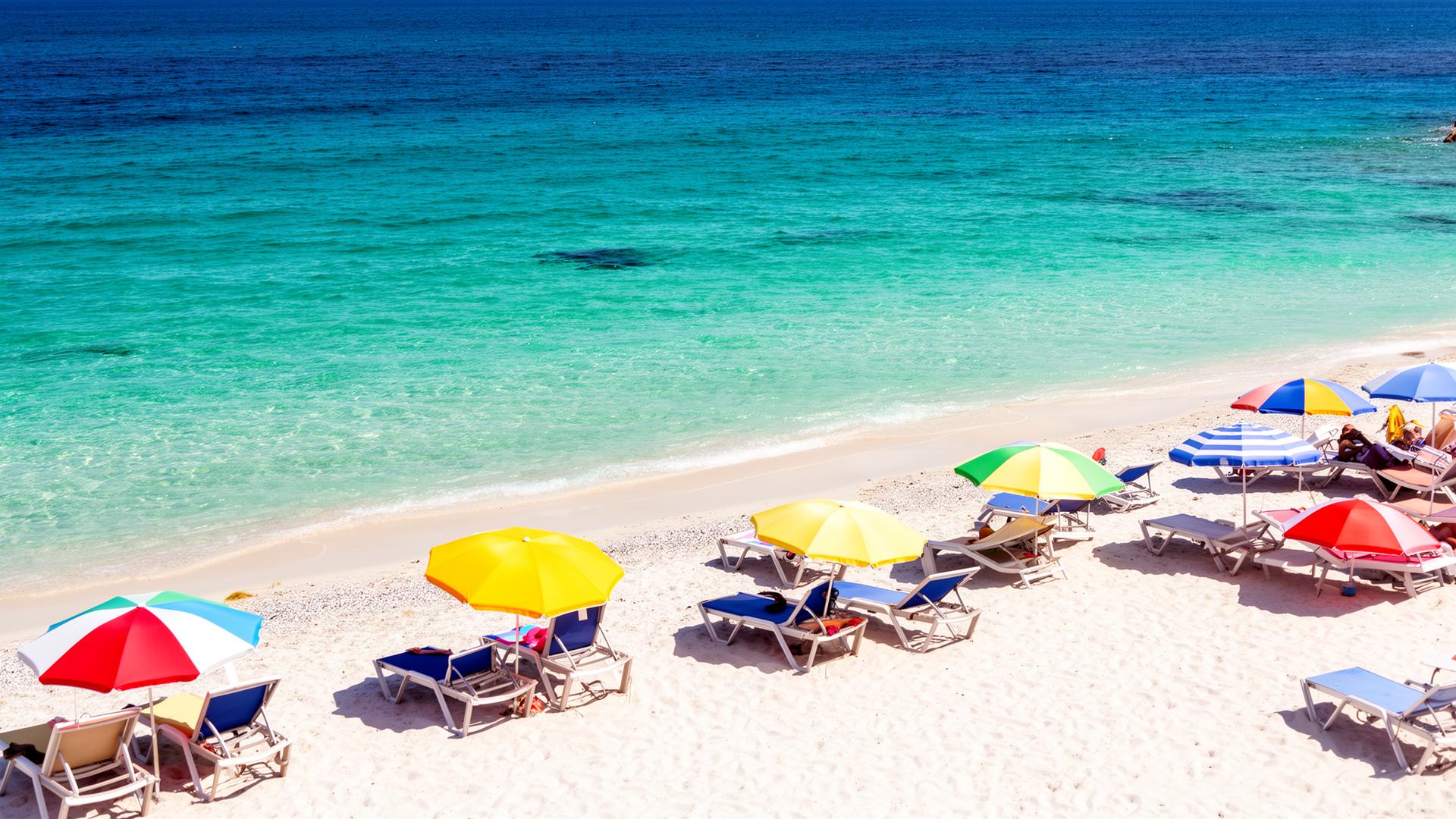 Zonnig strand met parasols en turquoise zee - grote vakantie juli augustus
